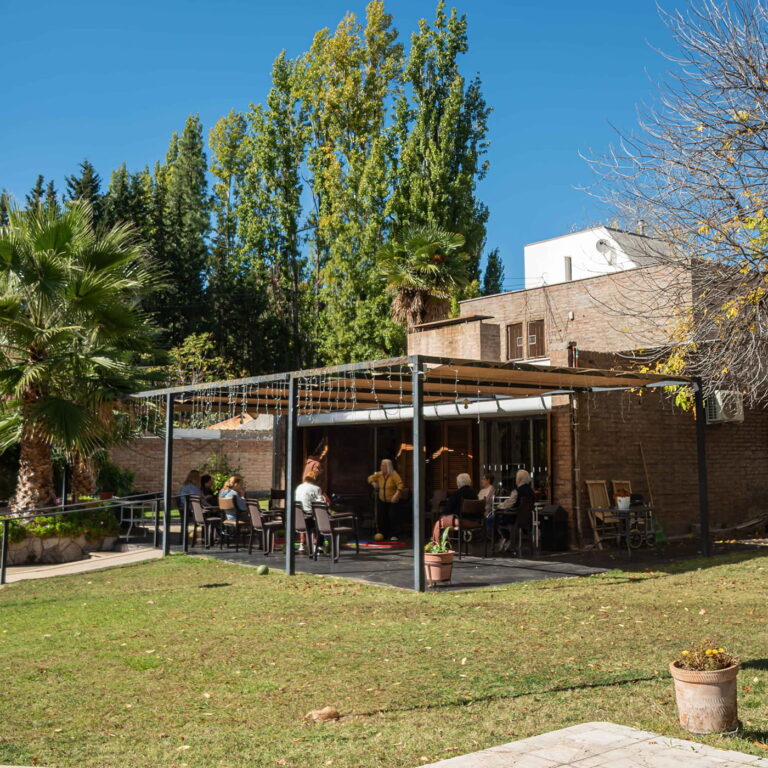 Mujeres mayores compartiendo un momento bajo la pérgola del jardín de Residencia La Flor de Chacras, en Chacras de Coria, Mendoza