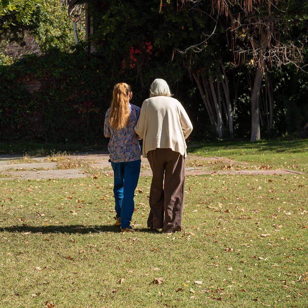 Cuidadora acompañando a una residente mayor en un paseo por el jardín de La Flor de Chacras